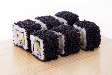 One set of California rolls covered black tobiko or masago caviar on a wooden board on a white background