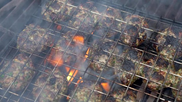 Closeup straight down on a grill with kofta cooking and smoke pouring off with flames.