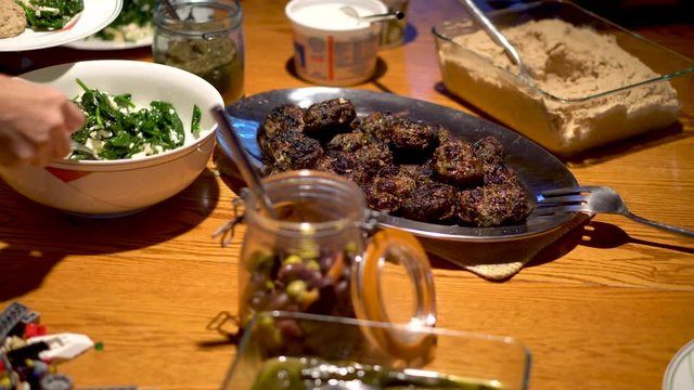 Cooked kofta as a centerpiece on a table while spinach and pine nuts are being served.