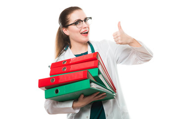 Attractive caucasian brunette female doctor standing in office with binders in her hands with thumb up on white background