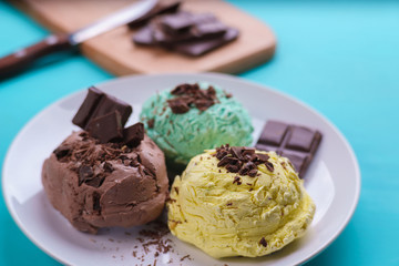 Mint, banana and chocolate ice cream scoops with chocolate crumbs served on white plate. Delicious refreshing summer sweets, close up