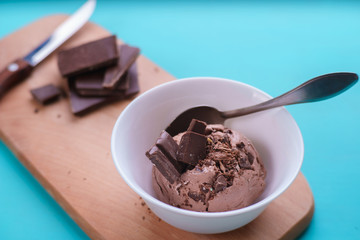 Chocolate ice cream in bowl and broken chocolate bar on serving board. Delicious summer treat close up
