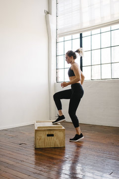 Side view of female athlete jumping on wooden box in gym
