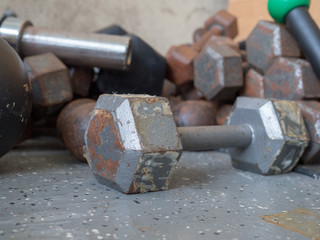 Peeling, rusty dumbbell sitting near stack of other weights in gym