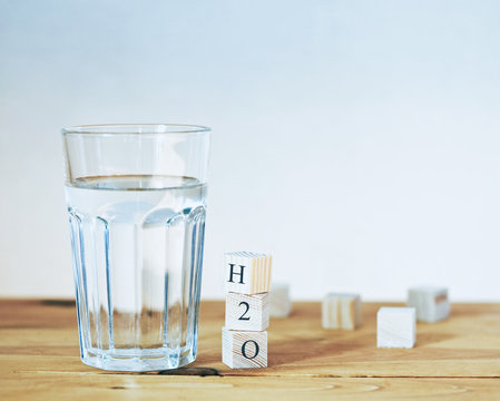 Glass of pure water with H2O formula written in wooden blocks