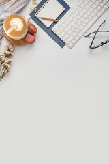 Flat lay, top view office table desk. Workspace with blank note book, keyboard, macaroon, office supplies, flowers, green leaf, gold ornament and coffee cup on white background.
