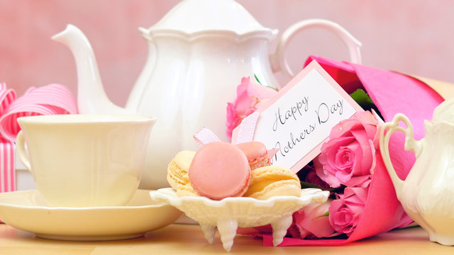 Happy Mother's Day tea setting with teapot, macaron cookies, pink roses and gift close up.