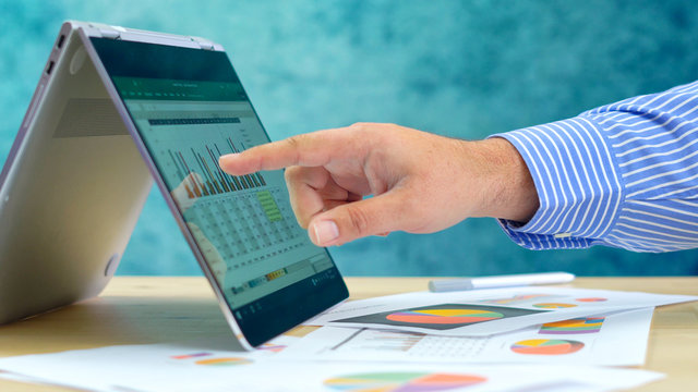 Businessman pointing and expanding graphs on modern touch screen technology laptop close up.