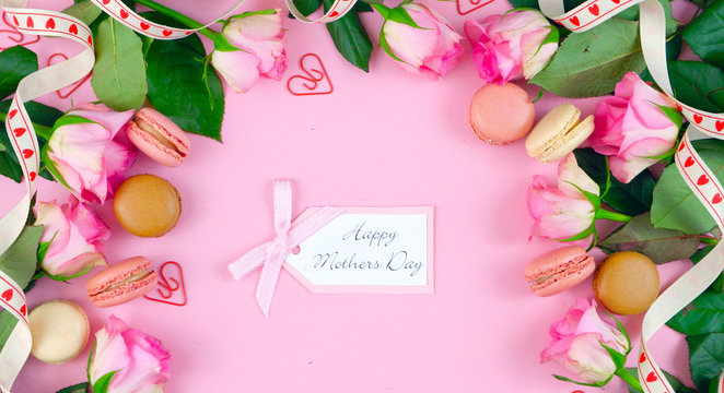 Happy Mother's Day background of pink roses and macaron cookies on pink wood table with gift card.