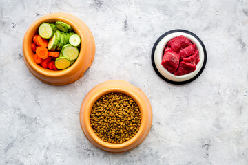 Dry pet food with natural ingredients. Raw meat, cut vegetables zucchini and carrot on stone backgroud top view copy space