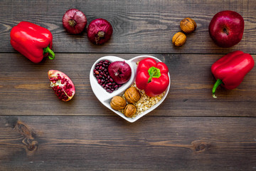 Proper nutrition for pathients with heart disease. Cholesterol reduce diet. Vegetables, fruits, nuts in heart shaped bowl on dark wooden background top view copy space