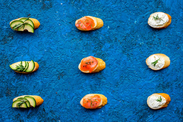 Fototapeta na wymiar Healthy lunch with mini sandwiches cheese, fish and avocado on blue background top view space for text