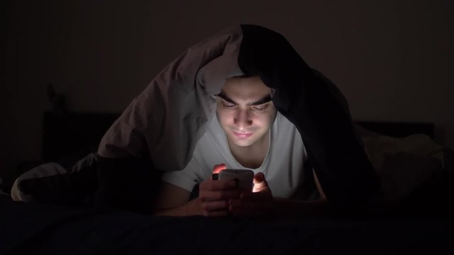 Man in his bed at night in the darkness using his smartphone