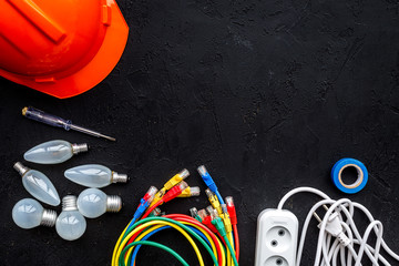 Electrician work concept. Hard hat, tools, cabel, bulb, socket outlet on black background top view space for text