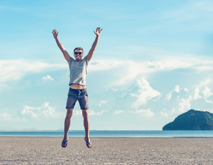 Obraz premium Happy young man jumping up on a beautifull the beach with sky clouds background. Freedom concept