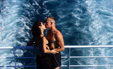 Attractive couple kissing and enjoy summer vacation. Honeymoon, just married concept. Couple stands on deck of cruise liner with sea waves on background. Couple in love travelling on cruise ship.