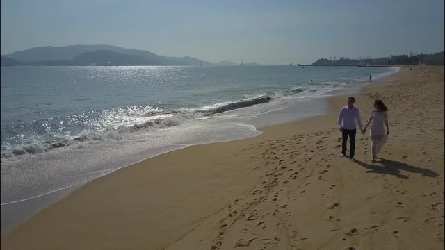 Couple Walks by Ocean Rolling Waves against Hills