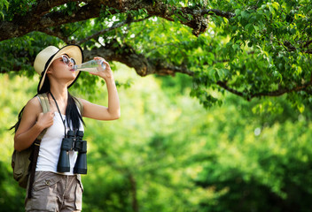Healthy and sporty young woman drinking water from the bottle against green of forest.