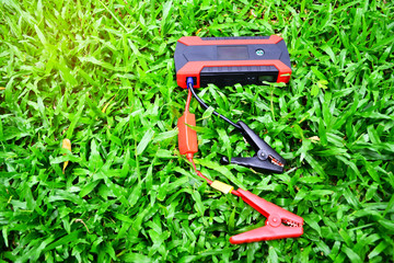 Car jump starter for emergency charger booster with power bank battery technology on the green grass background