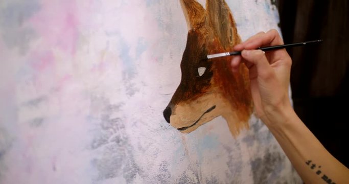 Artist paints picture on canvas with acrylic paints in her workshop. Girl artist draws a picture, fox muzle, closeup