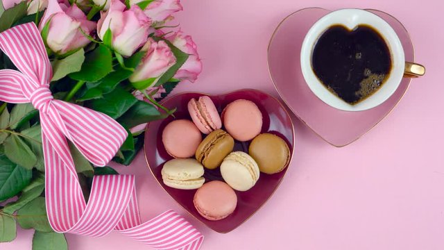 Serving Mother's Day coffee and macarons with roses gift overhead on pink wood table background.