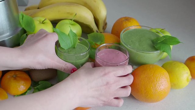 Female hands take a glass of smoothies from the table on the kitchen table