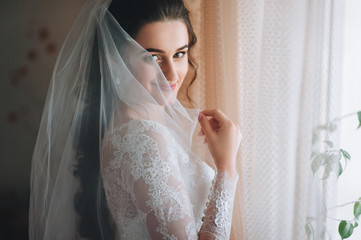 A beautiful and playful bride covers herself with a veil and smiles.
