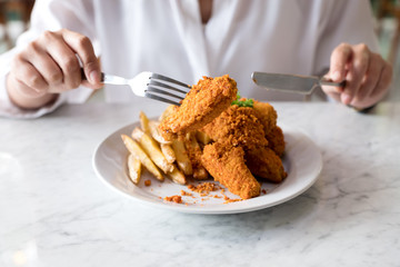 Closeup image of a hands using knife and fork to eating french fries and fried chicken in restaurant