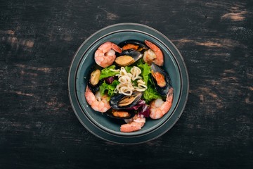 A plate of seafood. Mussels, squid, shrimp. Top view. On a black wooden background. Copy space.