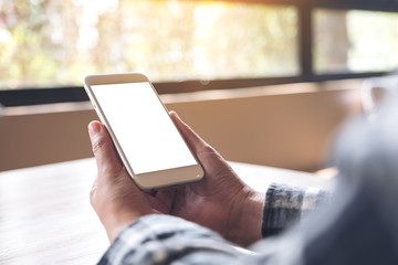 Mockup image of hands holding white mobile phone with blank desktop screen in cafe