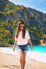 beautiful happy young woman wearing glasses and shorts resting on a turquoise beach, walking through the sand surrounded by beautiful nature, smiling and laughing, Fethiye, Oludeniz in Turkey