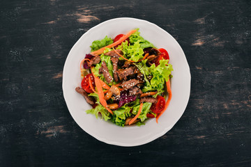 Vegetable salad with veal and mushrooms. On a black wooden background. Top view. Copy space for your text.