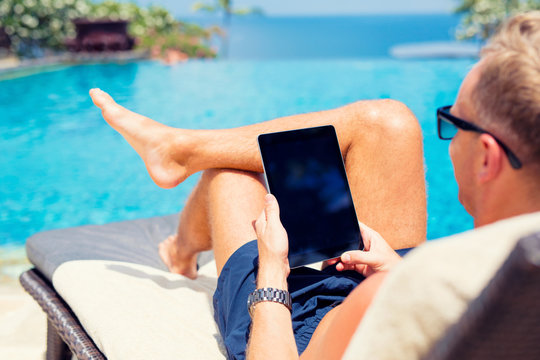 Man using tablet computer on vacation by the pool