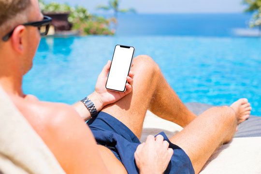Man by the pool holding mobile phone with empty white screen