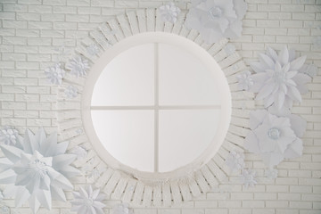 White background with brick wall, round window and paper flowers. Interior of the photo studio. Decor of paper