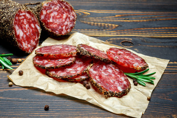 Dried organic salami sausage covered with pepper on wooden background