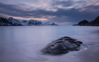 late evening landscape of lofoten, in blue tones with a big rock in foreground and mountains in background