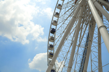 Fototapeta na wymiar Giant Ferris wheel with numbered cabins in the park - Bright blue sky with sharp clouds behind it.