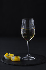 a glass of white wine on a black table with a fruit dessert