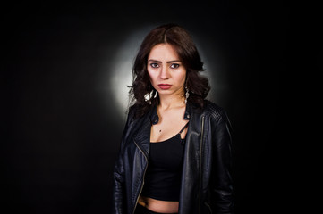 Studio portrait of sexy brunette girl in black leather jacket against black background.