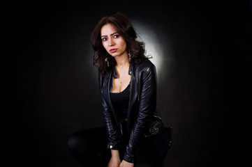 Studio portrait of sexy brunette girl in black leather jacket against black background.