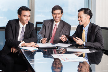 Three Asian Businessmen in conference room working over papers and contracts on desk