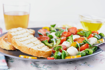 Fresh toasts and salad with cherry tomatoes, mozzarella balls, bell pepper and lettuce corn in a gray ceramic dish are ready for lunch