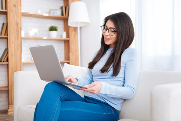 Self education. Reflective pretty female student sitting on sofa while studying with laptop