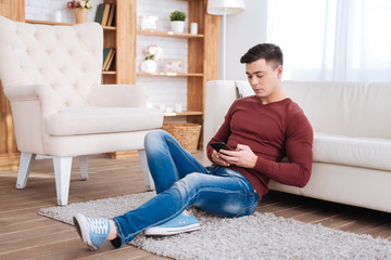 Active messaging. Attentive nice man gazing down while sitting on floor