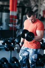 Muscular man training with black dumbbell in the gym