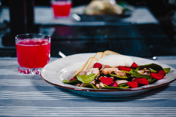 White plate with poached egg in salad with knife and fork. Next glass with red juice. Blue tablecloth on the background. Clouse up
