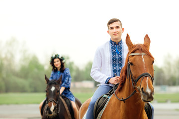 Fototapeta premium guy sits on a horse and looks at the camera lens on the background of his girl who sits on a horse
