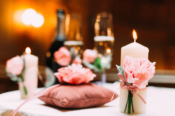 lighted candle is decorated with peonies and in the background champagne with glasses and a small pillow with flowers