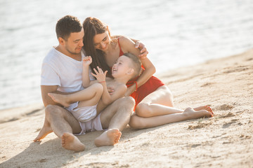 Fototapeta premium Happy family having fun at the beach. Mom, dad, son and little daughter at the sea shore. Cheerful family